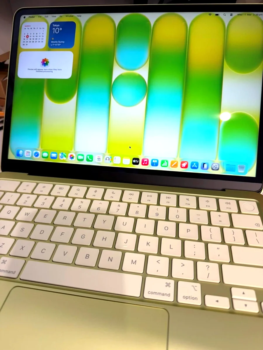 MacBook Neo first boot showing macOS desktop with widgets and citrus colour keyboard visible below the screen